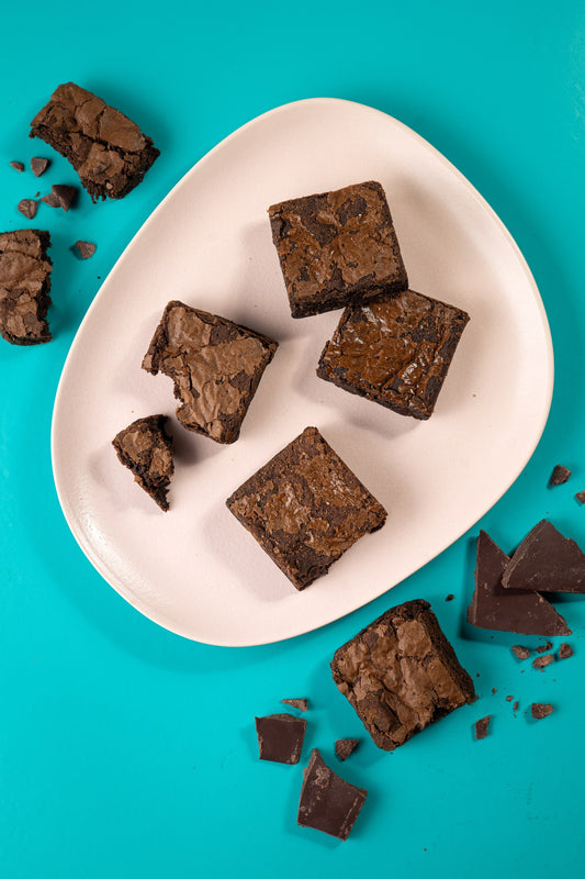 Pedaços de brownie sem glúten em prato branco sobre fundo turquesa, com lascas de chocolate