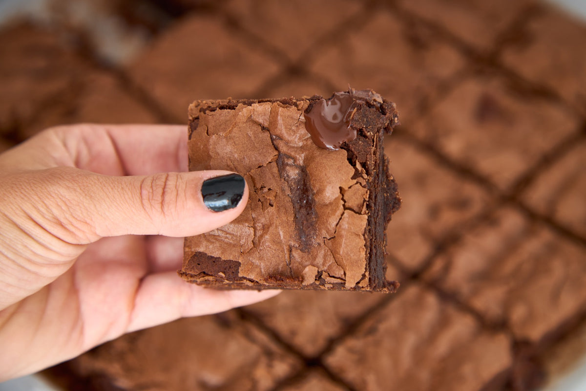 Mão segurando um pedaço de brownie, mostrando o miolo úmido e a casca craquelada
