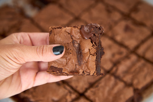 Mão segurando um pedaço de brownie, mostrando o miolo úmido e a casca craquelada