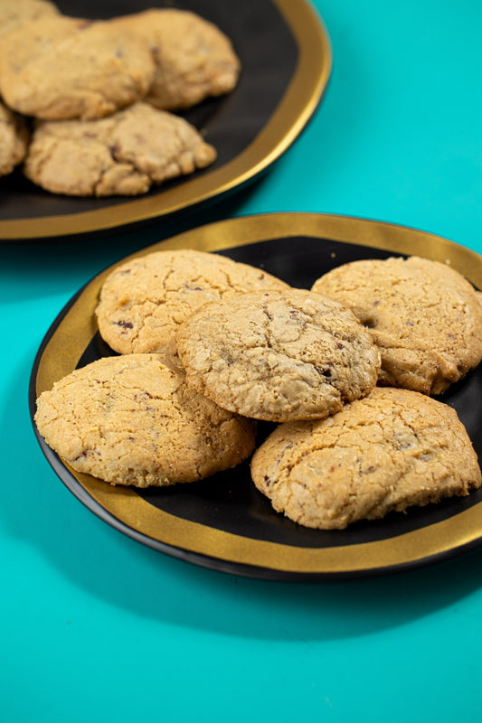 Cookies com pedaços de chocolate em prato preto e dourado sobre fundo turquesa