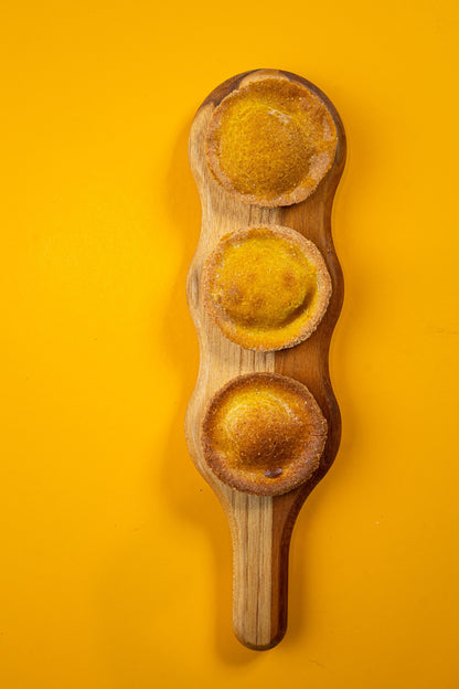 Três empadas de frango inteiras sobre tábua de madeira, fundo amarelo