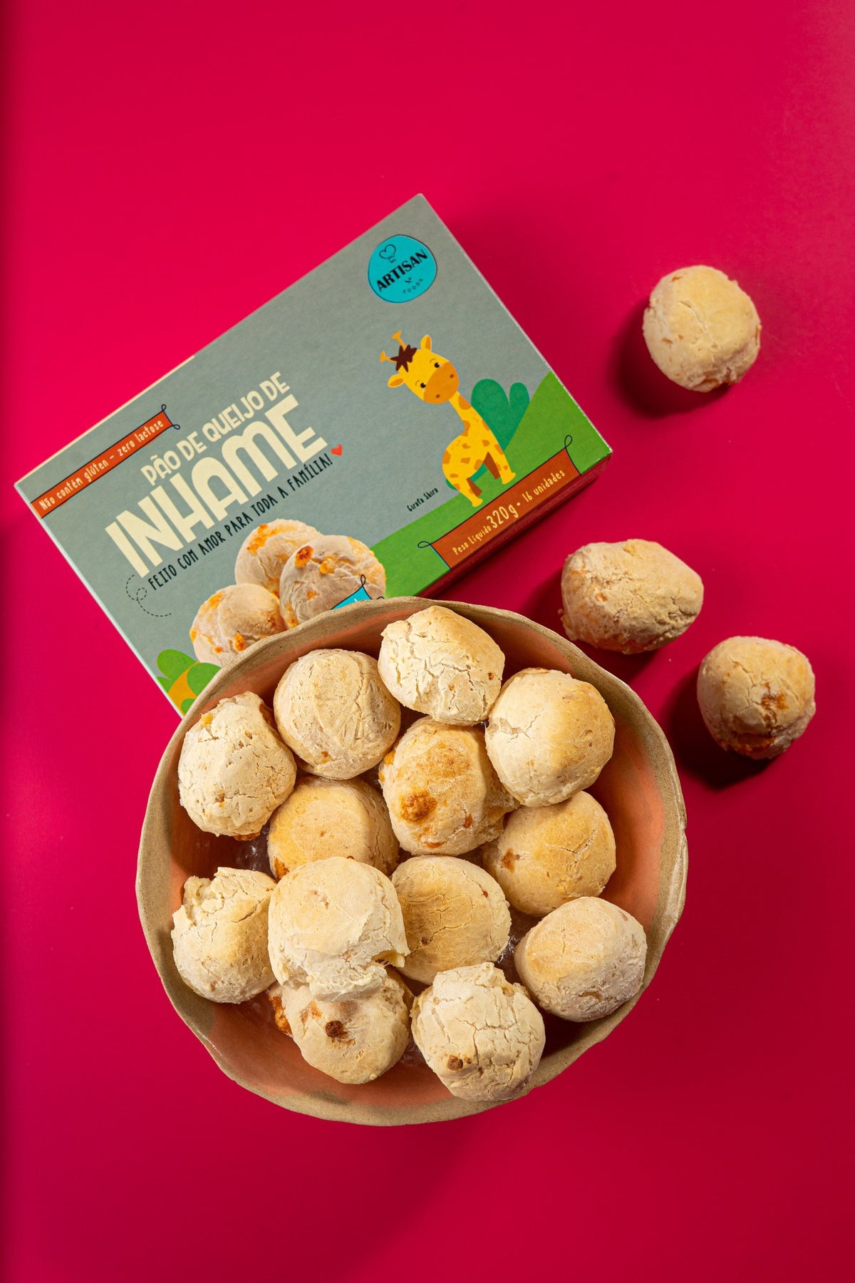 Caixa de pão de queijo de inhame ao lado de uma tigela de madeira com os pães, fundo carmim