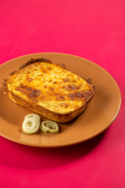 Quiche de queijo com alho-poró em prato laranja sobre fundo carmim