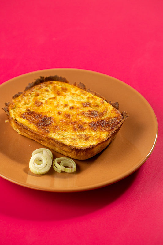 Quiche de queijo com alho-poró em prato laranja sobre fundo carmim
